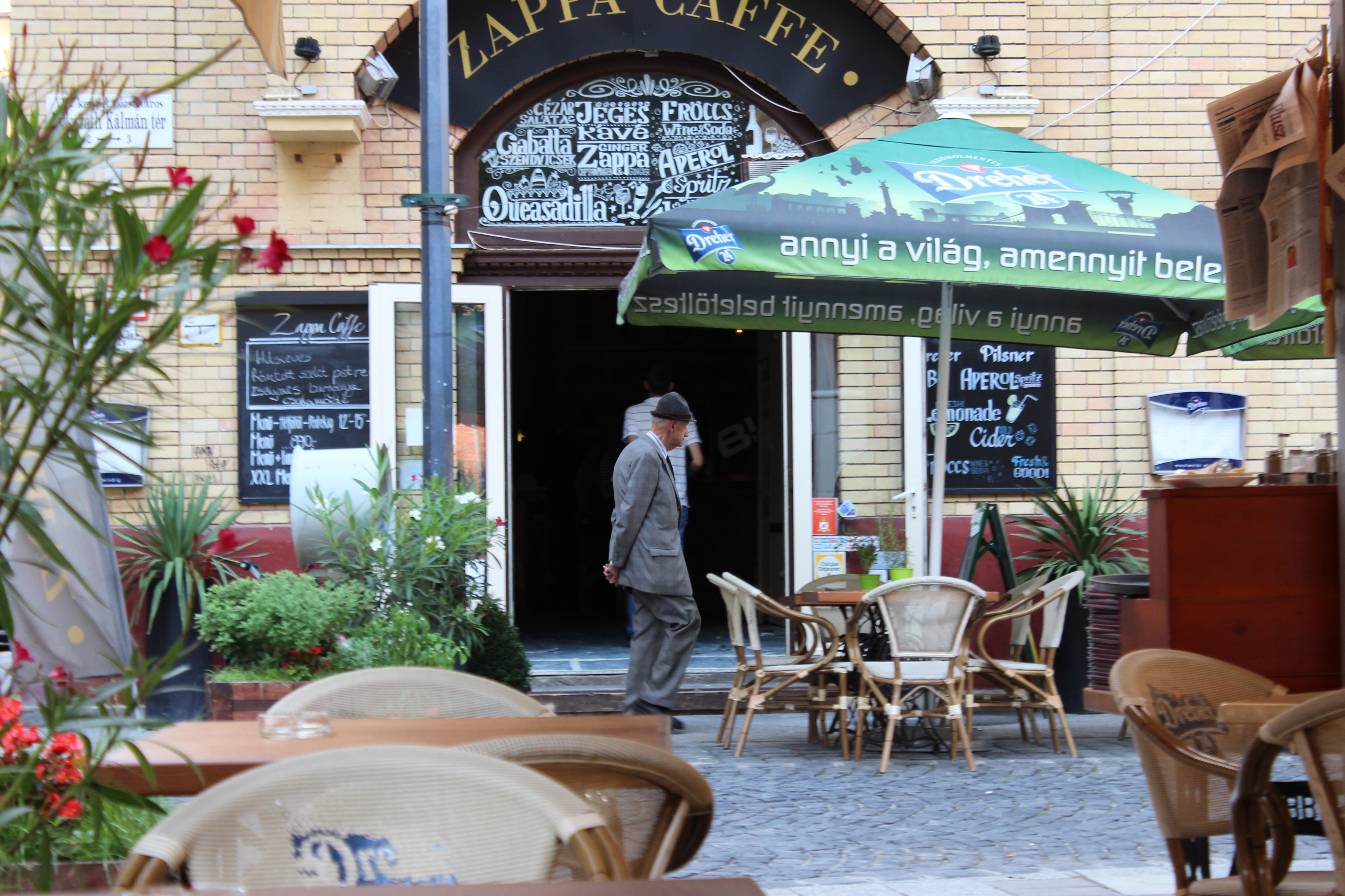 An older gentleman in a suit and hat passes a café terrace, Budapest